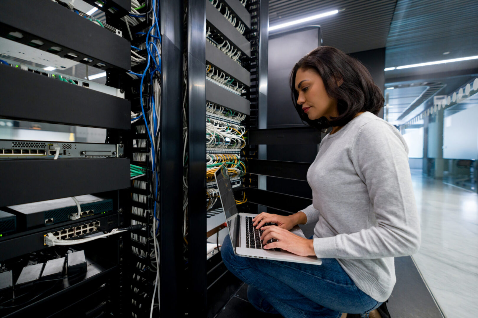 Woman working on a laptop near servers.