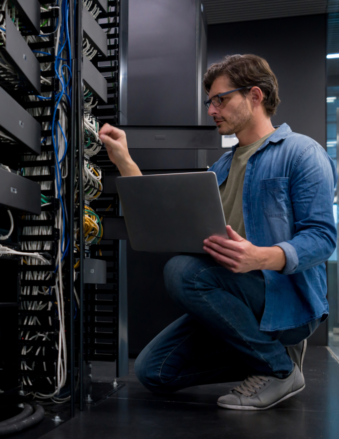 Technician working on server rack with laptop.